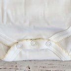 Body infantil blanco con ribete picot amarillo y botones a presión