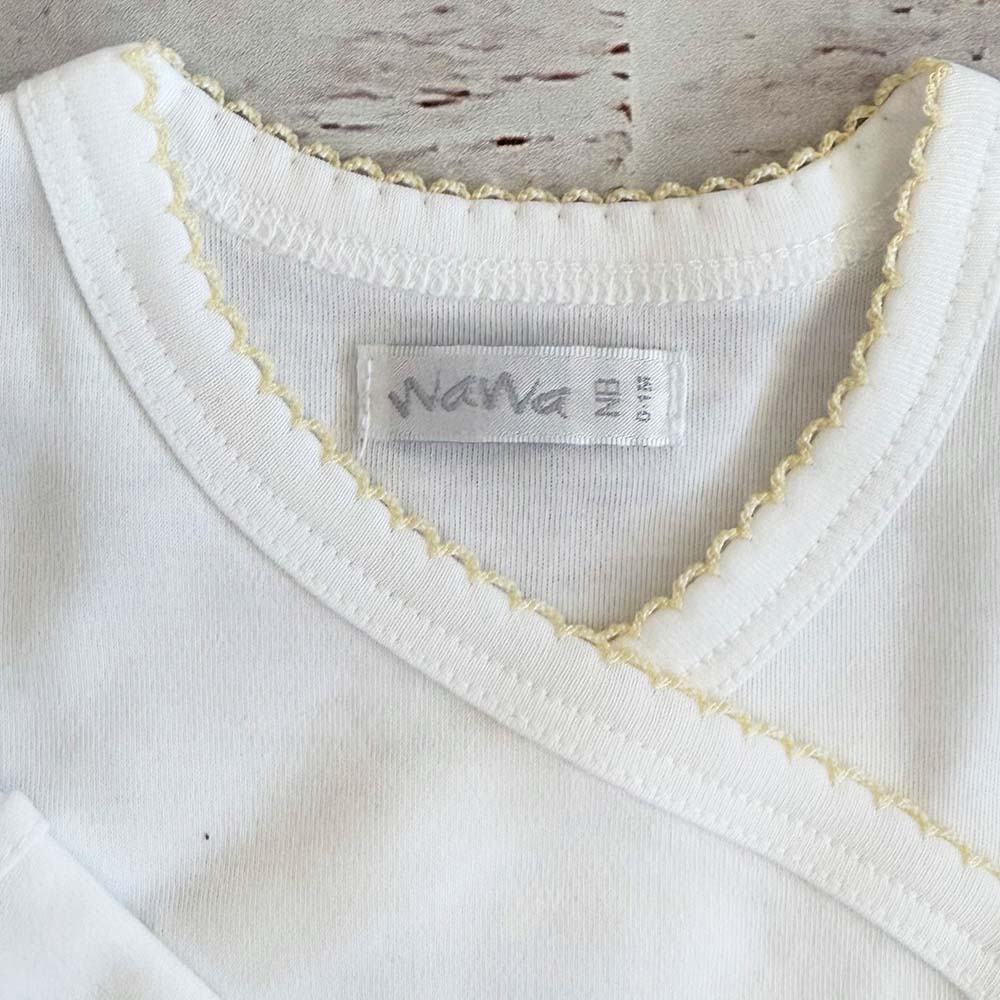 Cuello del body infantil blanco con ribete picot amarillo y etiqueta interior