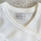 Cuello del body infantil blanco con ribete picot amarillo y etiqueta interior