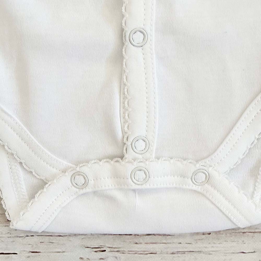 Body blanco para bebé con costuras elásticas en el bajo y broches