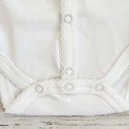 Body blanco para bebé con costuras elásticas en el bajo y broches
