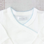 Body infantil blanco con escote en V y ribete celeste picot; etiqueta en el cuello