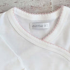 Cuello de body blanco con ribete picot rosado y etiqueta interior