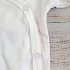Abertura lateral del body blanco con botones a presión y borde picot rosado