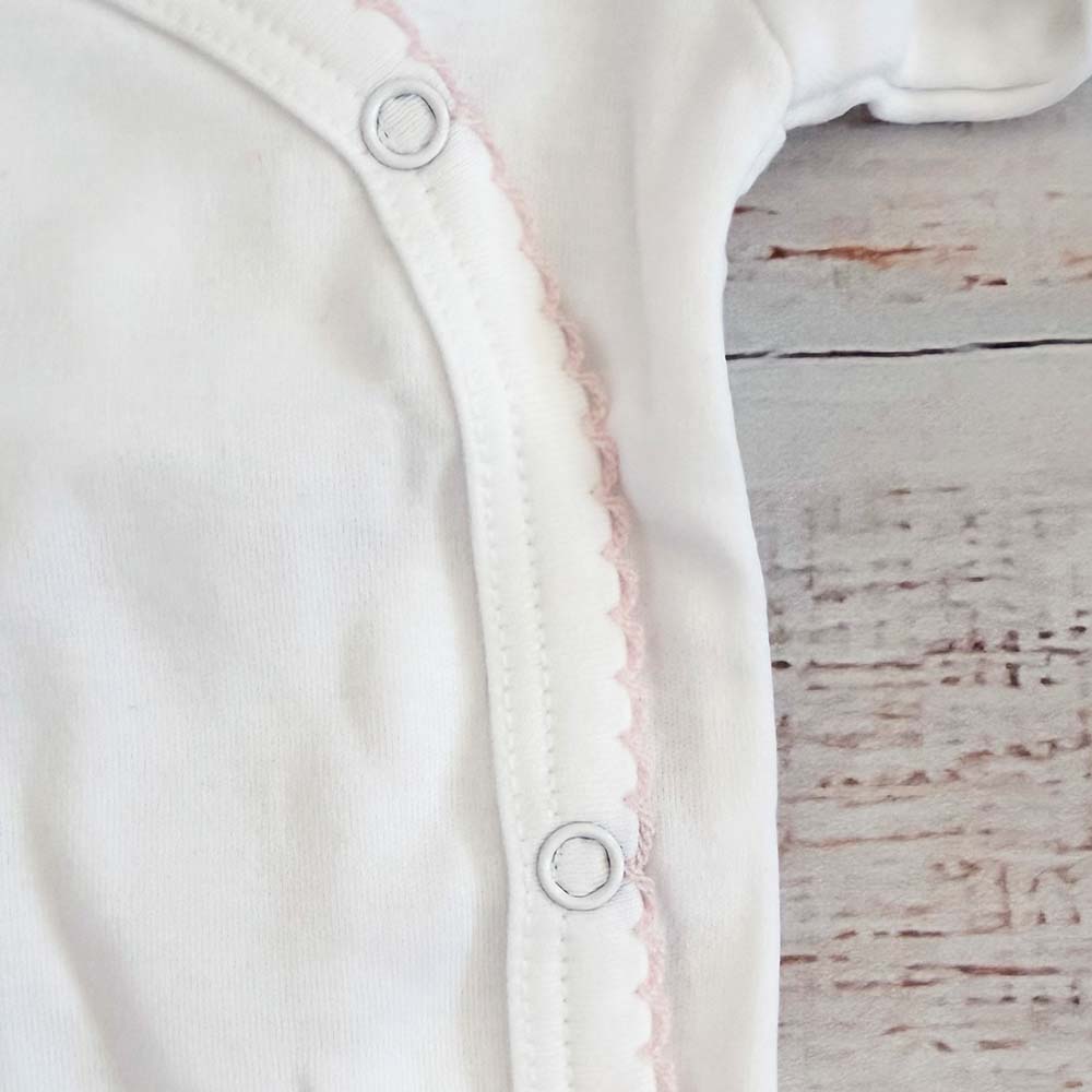 Abertura lateral del body blanco con botones a presión y borde picot rosado