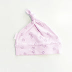 Gorro infantil rosado con nudo en la parte superior y estampado repetido de coronas.