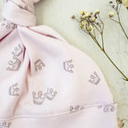 Gorro infantil rosado con estampado de coronas, nudo superior y costura en el borde.