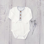 Body infantil blanco de manga larga con tapeta a rayas grises y botones de madera