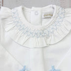 Body blanco con cuello de volante y fruncido, lazos celestes y botones al hombro.