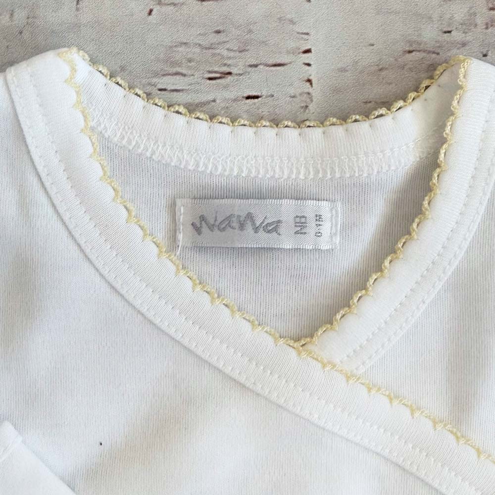 Detalle de cuello redondo del body blanco con borde picot amarillo y etiqueta interior
