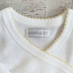 Detalle de cuello redondo del body blanco con borde picot amarillo y etiqueta interior