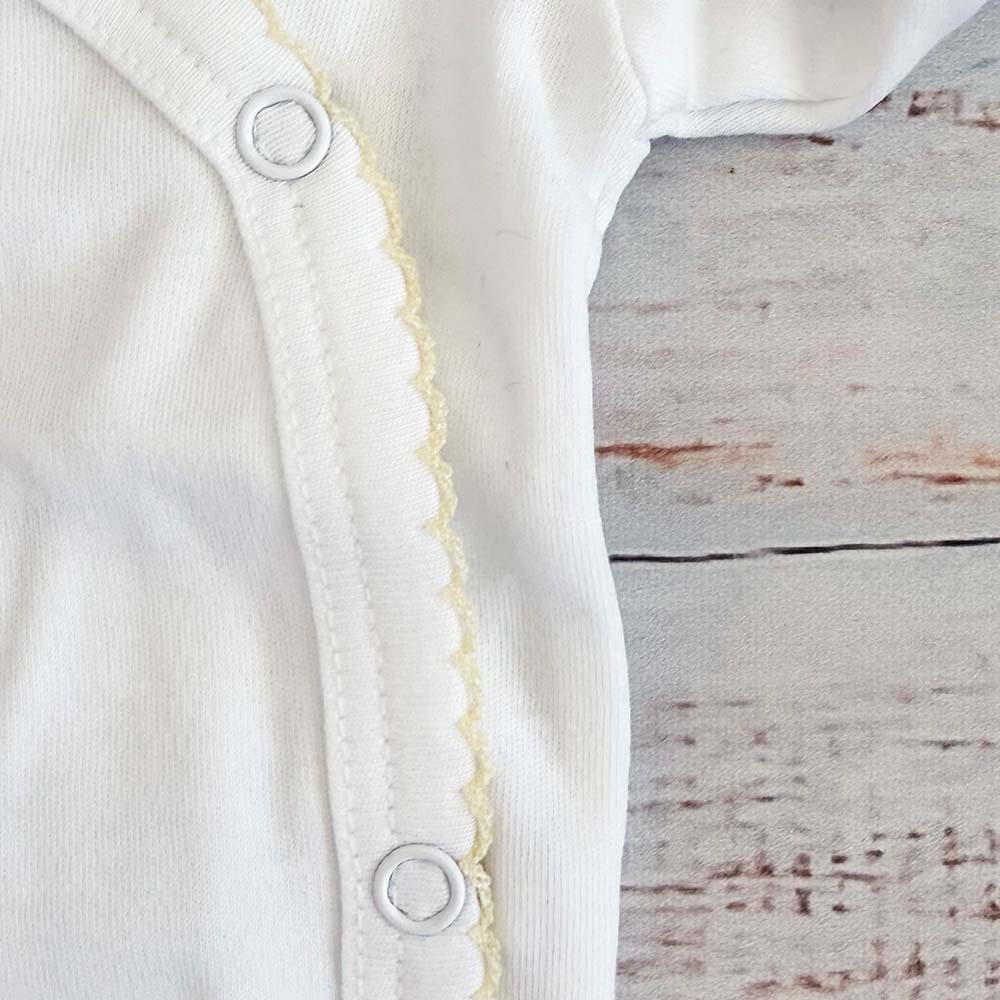 Detalle lateral del body blanco con cierre a presión y borde picot amarillo