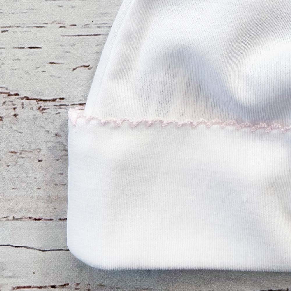 Detalle de manopla: tejido blanco y borde con puntilla rosa