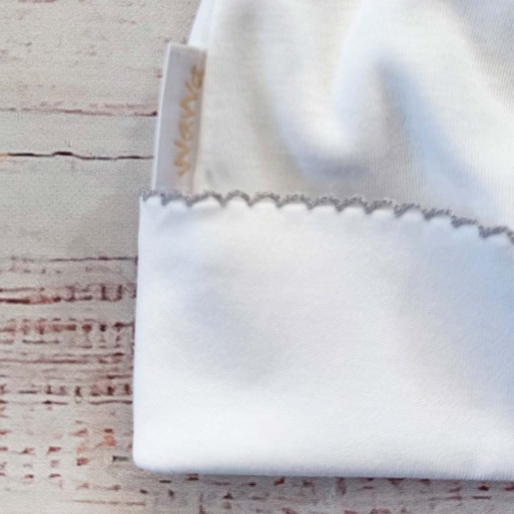 Detalle de gorro de bebé blanco con etiqueta interior y borde ondulado