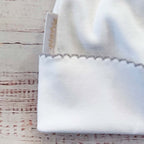 Detalle de gorro de bebé blanco con etiqueta interior y borde ondulado