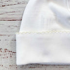 Detalle del borde fruncido de gorro blanco de recién nacido con acabado irregular