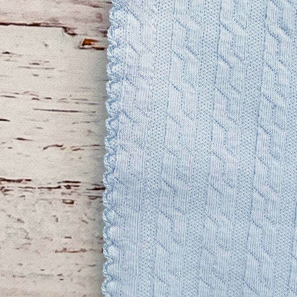 Detalle de tela jacquard celeste con textura y ribete cosido, esquina