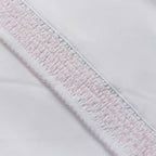 Detalle de borde y puntadas smock con hilo rosado sobre tela blanca
