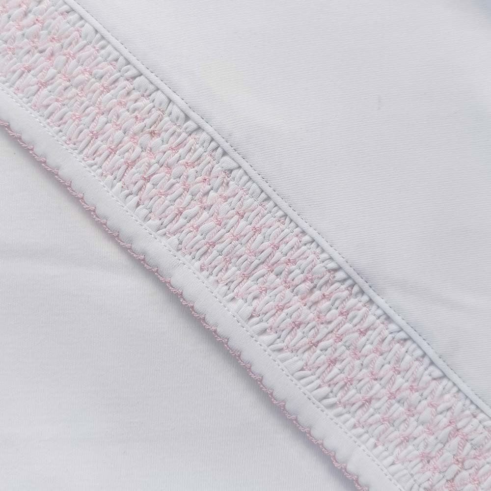 Detalle de borde y puntadas smock con hilo rosado sobre tela blanca