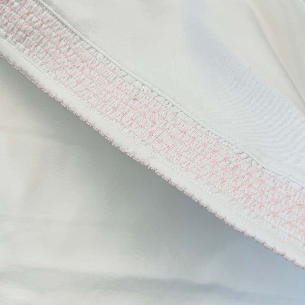 Borde inferior con franja smock rosada sobre tela blanca