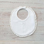 Babero de niña blanco con bordado calado y volante alrededor del cuello, cierre ajustable.