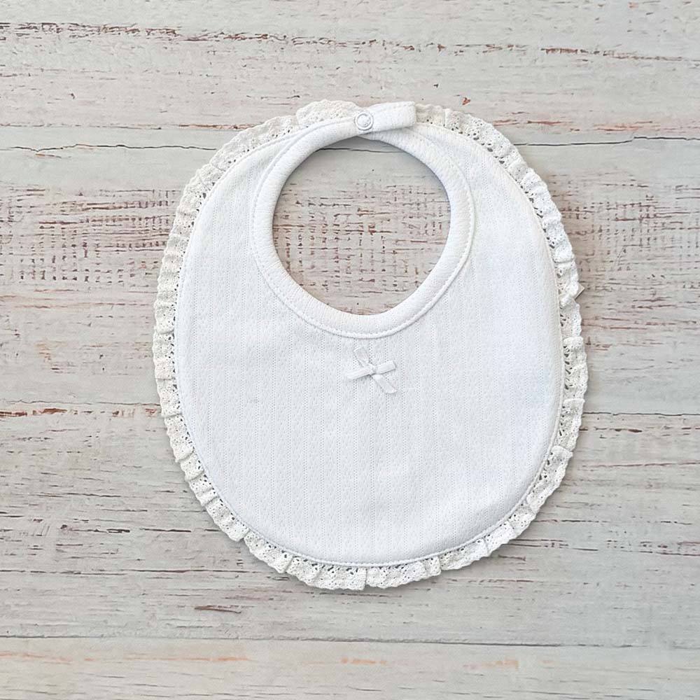 Babero de niña blanco con bordado calado y volante alrededor del cuello, cierre ajustable.