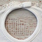 Babero de niña blanco con ojal circular y volante calado en el contorno del cuello.