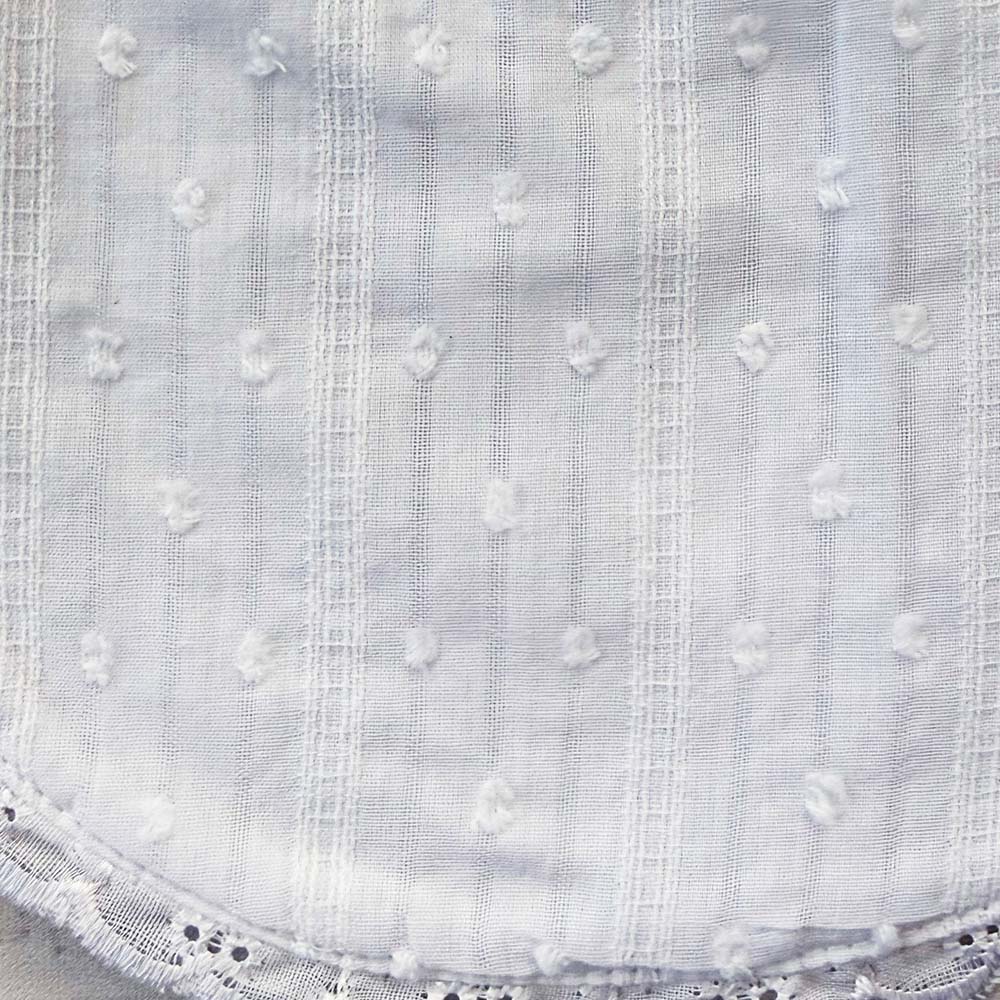 Babero blanco bordado con líneas verticales y relieve de puntitos en la tela
