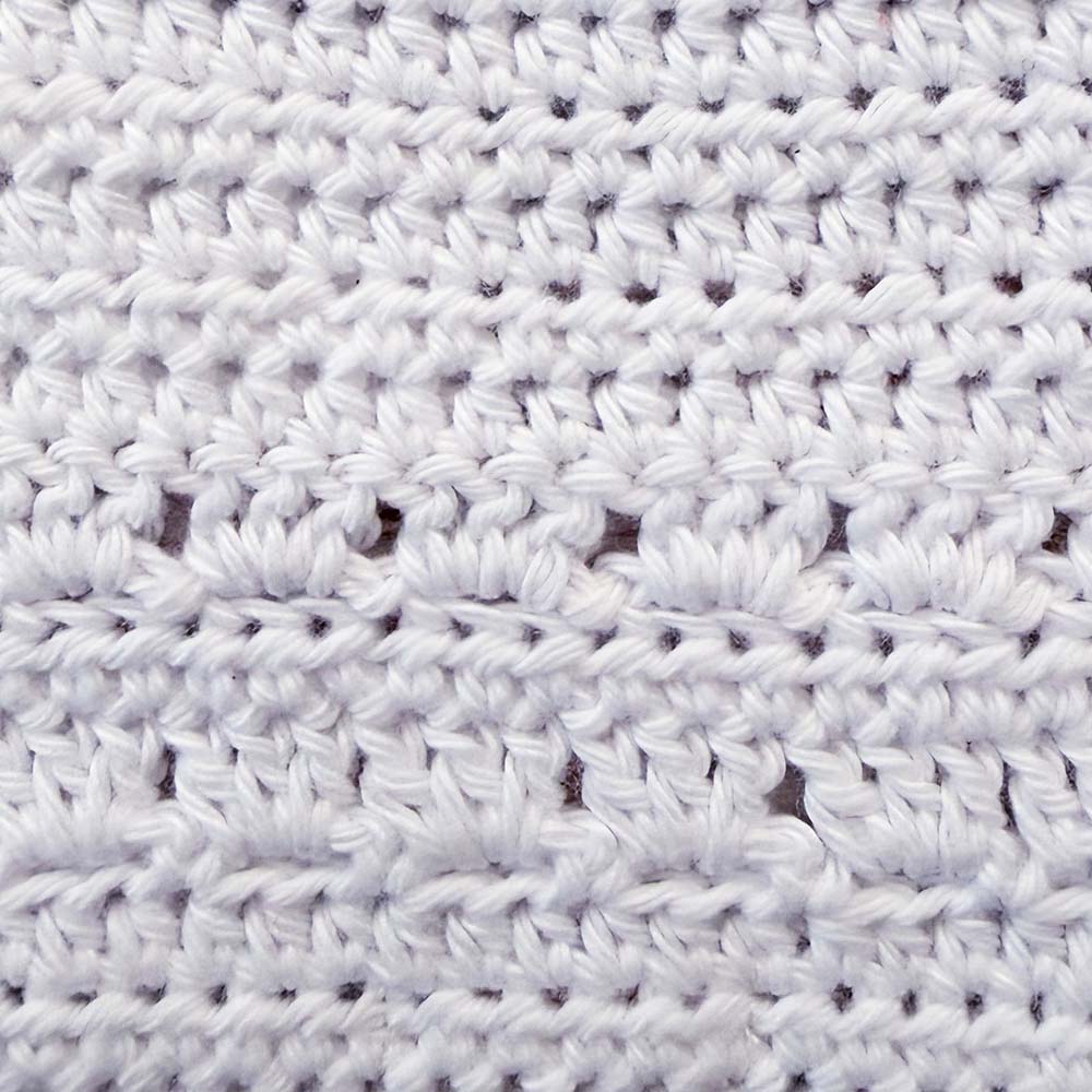 Babero de crochet blanco con patrón de puntos en relieve y líneas horizontales