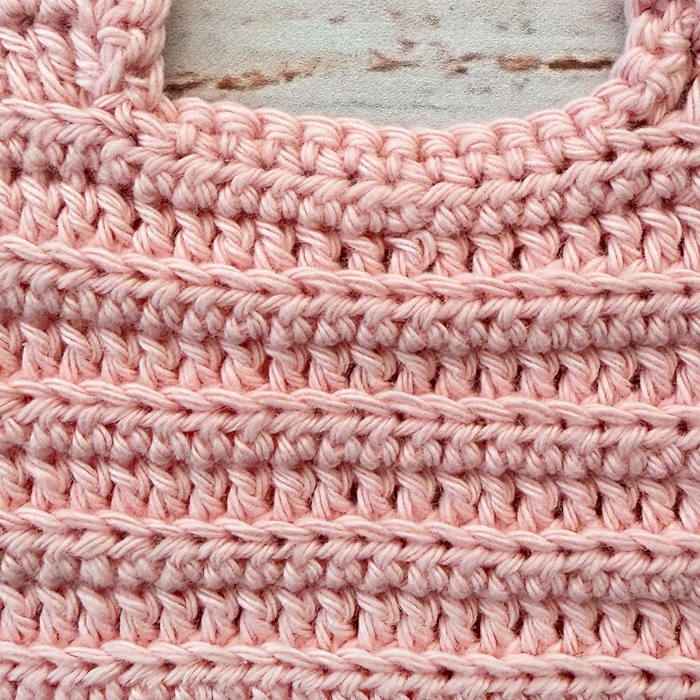 Babero de crochet rosado con textura uniforme y borde superior reforzado