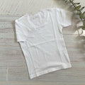 Camiseta blanca básica de niña con manga corta, cuello redondo y adorno pequeño frontal.