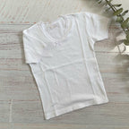 Camiseta blanca básica de niña con manga corta, cuello redondo y adorno pequeño frontal.